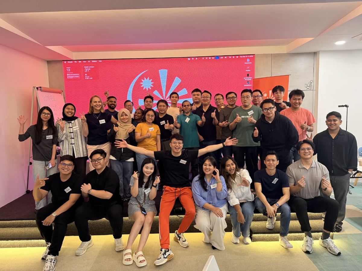 Workshop attendees on stage in front of a large red screen, smiling and giving thumbs up